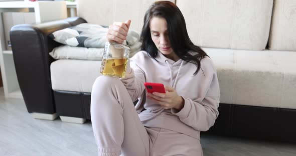 Woman with Bottle of Alcohol and a Smartphone is Sitting on Floor