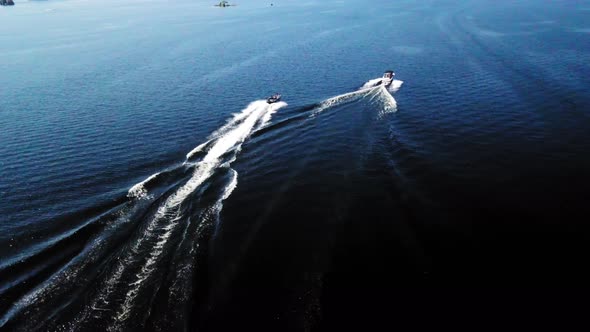 4K aerial shot of motor boats speeding along a blue lake on a sunny day.