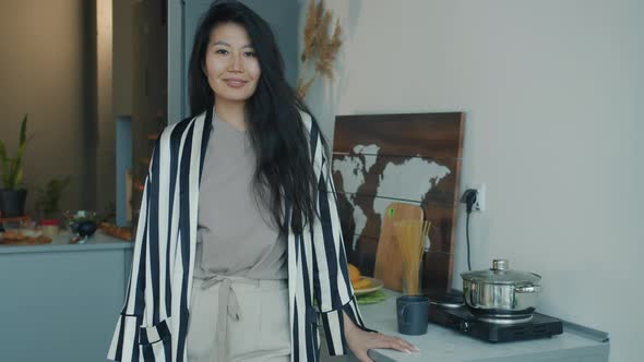 Slow Motion Portrait of Cheerful Asian Woman Standing in Kitchen at Home Wearing Domestic Clothing