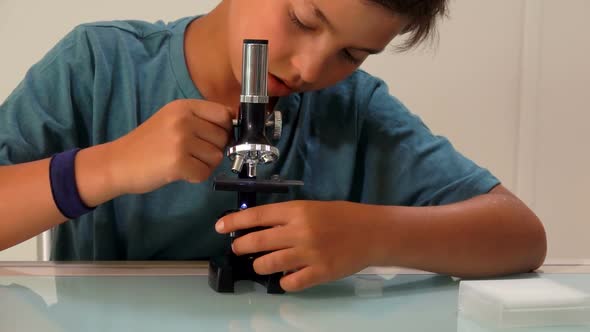 A Serious Teenage Boy is Lookings Through a Microscope