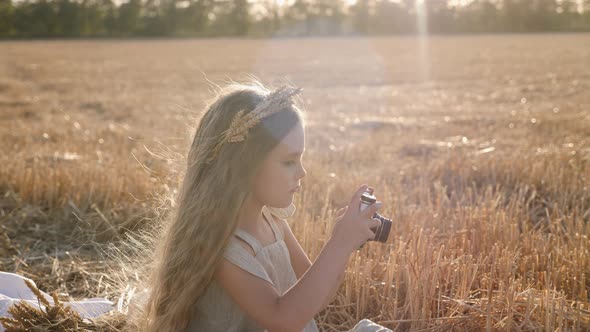 Serious Child Girl with Long Hair Sits on a Mown Wheat Field