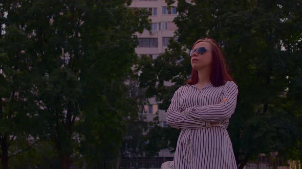 Young Woman in Sunglasses Standing on City Street and Looking Away