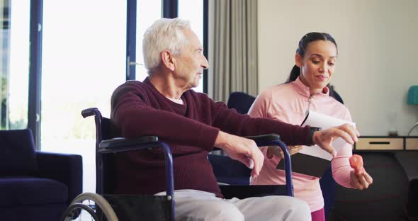 Video of happy biracial female physiotherapist exercising with caucasian senior man