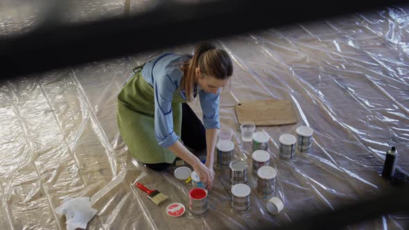 Woman in Studio Workshop Open Different Colors of Paint in Metal Jars on the Floor