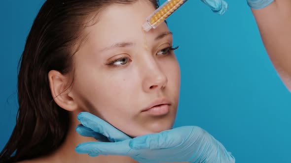 Cosmetology Doctor in Blue Gloves Holding Woman Face and Carefully Applying Orange Liquid with