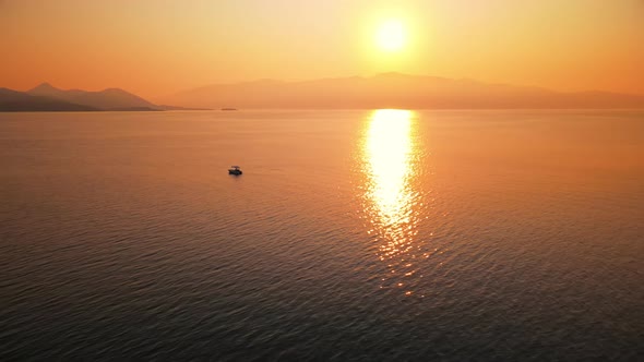 Sunset on the Ionian Sea coast, Greece. Bright Sun, land in the distance, floating boat