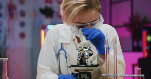 Woman Chemist in Protective Mask, Eyewear and Gloves Learning Samples Under microscope