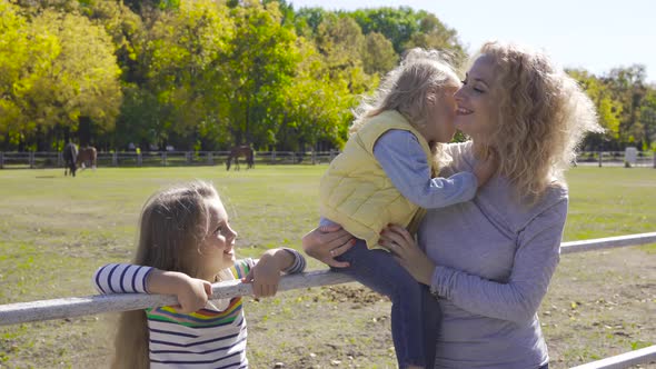 Two Cute Little Sisters Spending Time with Their Lovely Mom Next To the Corral