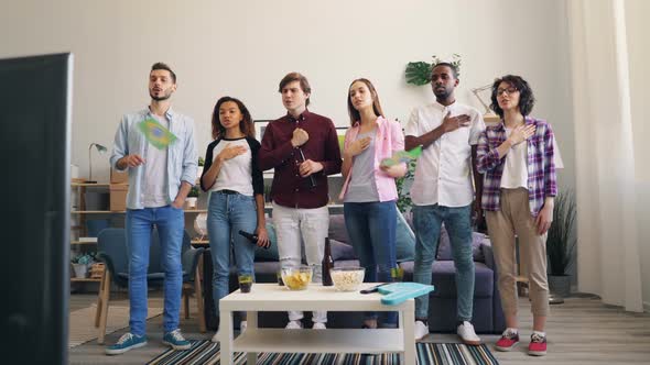 Brazilian Youth Singing Anthem at Home Watching Sports Game on TV Waving Flags