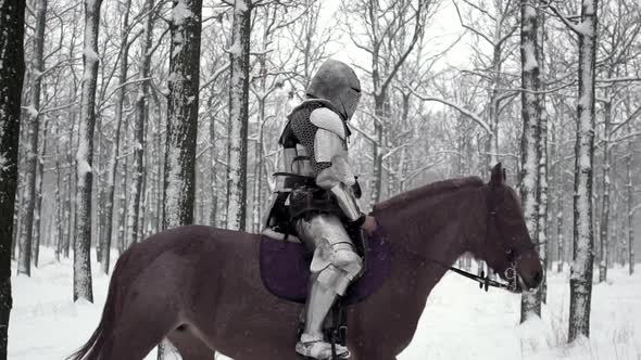 Lone Medieval Soldier Armed with Steel Weapon Riding on Dark Horse Through Winter Forest Under