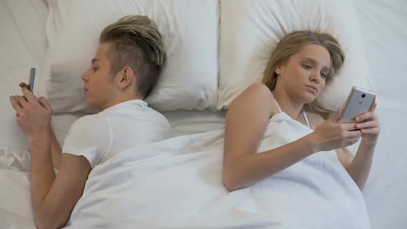 Couple Lying Back to Back in Bed With Smartphones