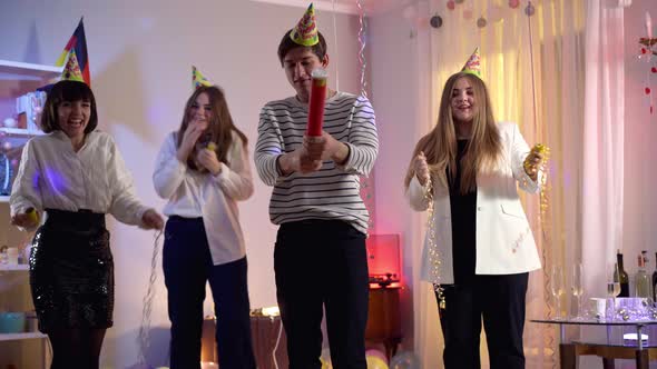 Wide Shot of Smiling Young Millennial Man Blowing Up Confetti As Cheerful Women Cheering