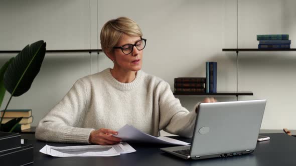 Portrait of a Mature Businesswoman Working at a Laptop in the Workplace in the Office Takes Off Her