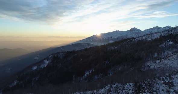 Forward Aerial Top View Over Winter Snowy Mountain and Woods Forest at Sunset or Sunrise