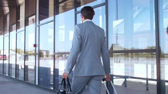 Elegant businessman walking with suitcase along the airport. Young mail entrepreneur.