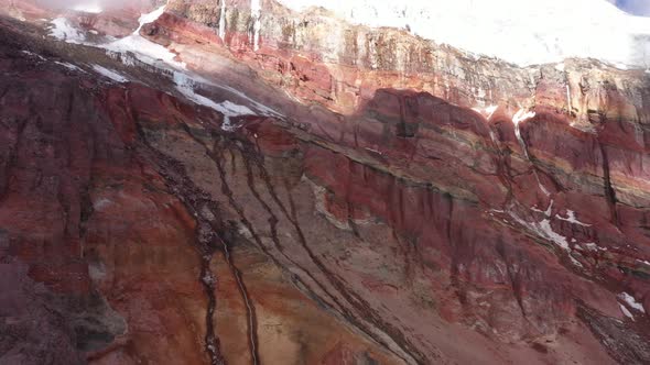 Aerial view of start of a gletser with loads of snow fallen down on the colorful rocky slopes below