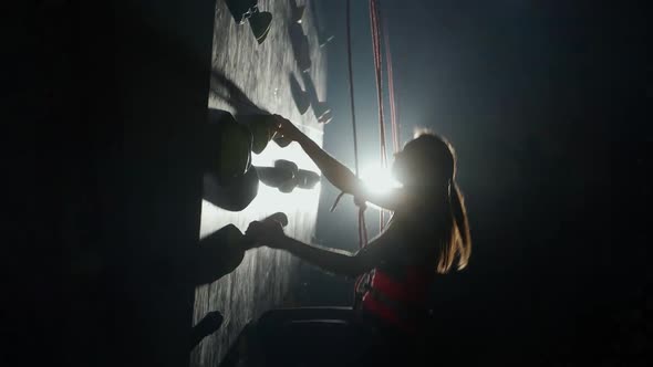 Female Climber Training on a Climbing Wall Practicing Rockclimbing and Moving Up Climbs the Cliff