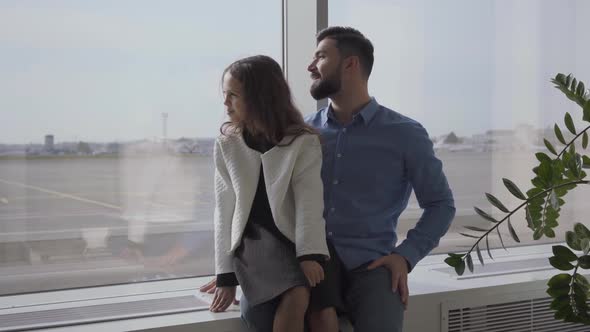 Happy Caucasian Father and Daughter Sitting at the Airport Windowsill and Looking at the Runway