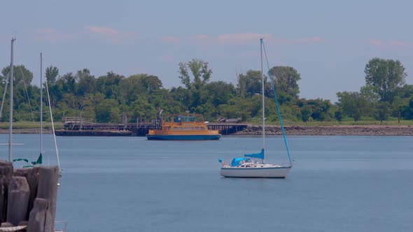 Roll-on, roll-off orange ferry heading to Hart Island, boats and dock in the foreground. Blue sky on