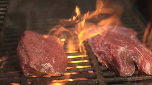 Two juicy pieces of raw meat are roasted on a hot grill over an open flame. BBQ.