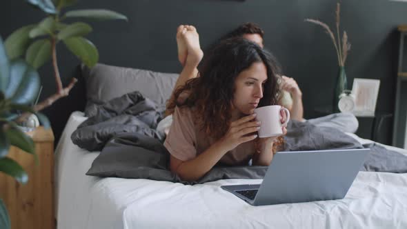 Couple Using Laptop and Smartphone in Bedroom