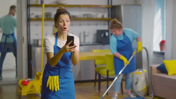 Woman Maid Winning Video Game on Smartphone and Celebrating with Colleagues Working on Background