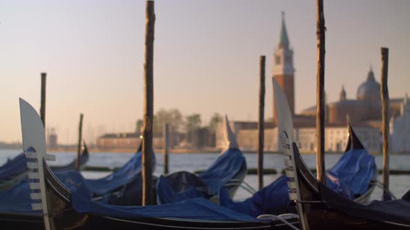 A Closeup of Covered Gondolas Swaying on a Pier Against the Blurred Venice View