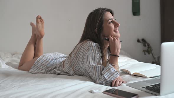 Happy young attractive woman lying on her bed smiling