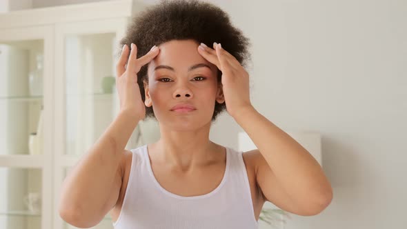 African american woman makes herself a face lifting massage in front of camera at home.