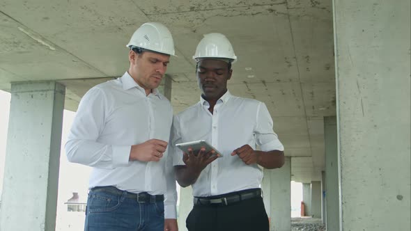 African American Engineer and Caucasine Architect Using Digital Tablet and Wearing Safety Helmets at