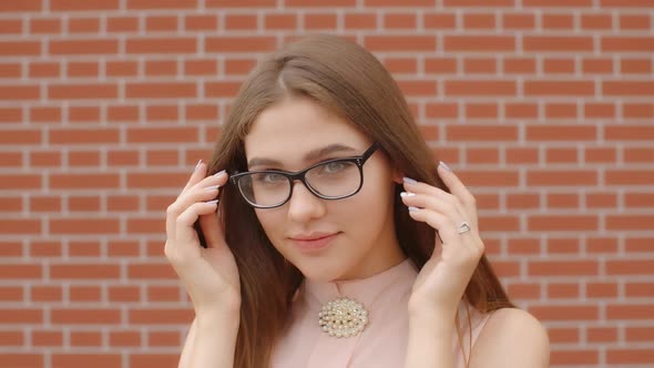 Student Girl Smiles, Takes Off Her Glasses and Fixes Her Hair Against Red Wall Background