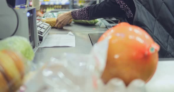 Buyer Puts the Products at the Checkout. Female Cashier Punches Vegetables and Fruits