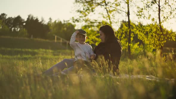 Mom Sits with Her Son on the Grass in the Park with Beautiful Nature