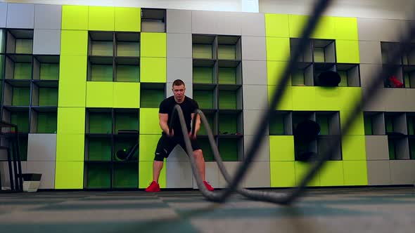 Young and Handsome Male Athlete Man Doing Exercises for the Muscles of the Body with a Battle Ropes