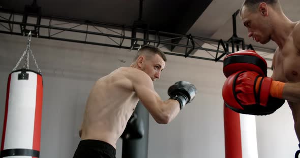 Low Angle Shot Fighter in Boxer Gloves is Practising His Strikes with Trainer in Slow Motion in the