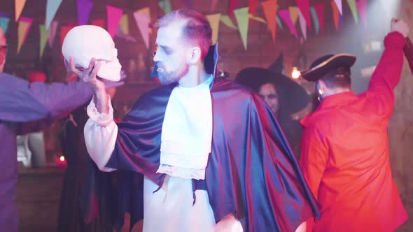 Man Disguised As a Vampire Dances with a Skull in His Hand