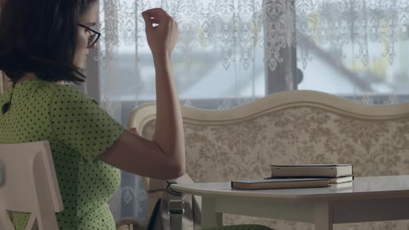 A Girl with Glasses and a Green Dress Sits at Her Desk and Reads Messages on Her Phone Side View