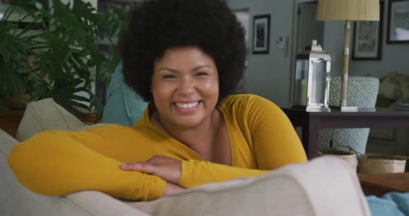 Video of happy plus size african american woman sitting on sofa