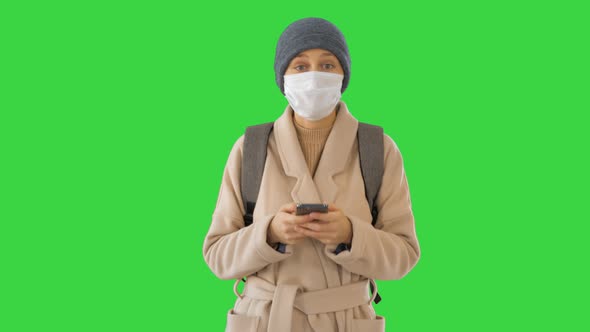 Woman Dressed in a Coat Wearing Medical Mask Using Phone and Walking on a Green Screen, Chroma Key.