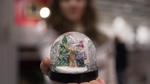 Young Woman Shows Festive Ball with Small Decorations Inside