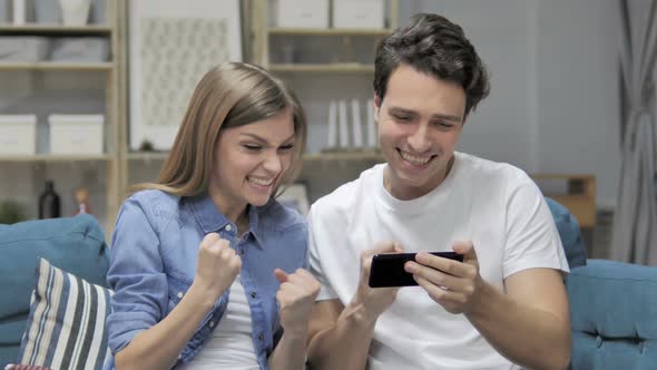 Cheering Young Couple Excited for Success While Watching on Smartphone