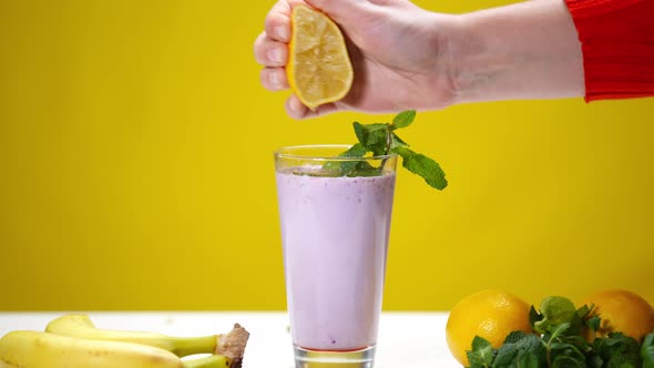 Female Hand Squeezing Halved Lemon in Purple Vitamin Smoothie in Slow Motion