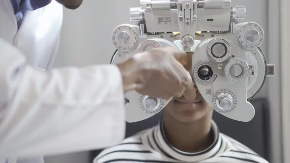 Optician doing optometry eye exam for black african american teen girl patient.