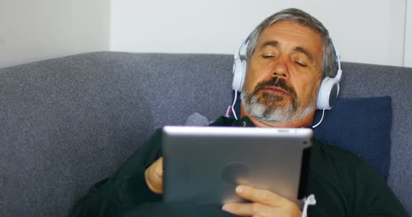 Man listening to music on digital tablet while lying on sofa 4k