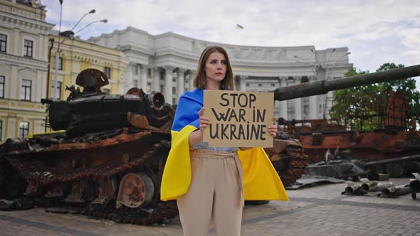 Woman Holds Poster Standing Against Big Tank on Square