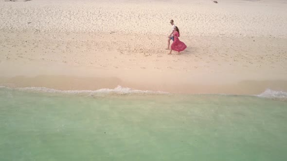 Aerial view of young caucasian couple walking on white sandy beach in Asia - static camera