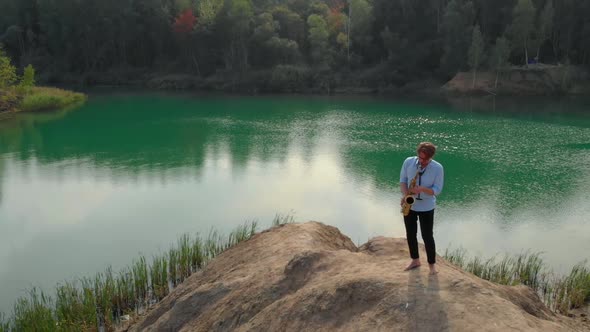 Amazing Landscape with Forest and Green Lake and Man with Saxophone on Hill, Aerial Shot