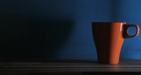 Close up clip of woman putting three orange cups on the wood table against blue background