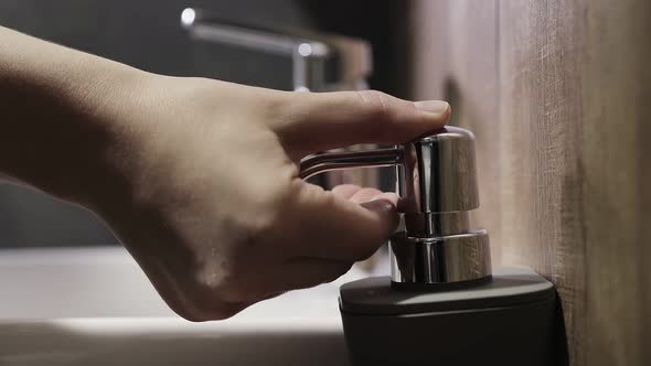 Woman pushes the dispenser and the liquid soap is squeezed in her hand.