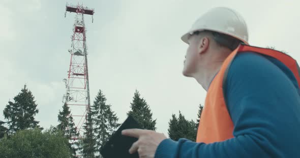 4G 5G Cellular Radio Tower Worker in Overalls and Helmet is Standing Next to It